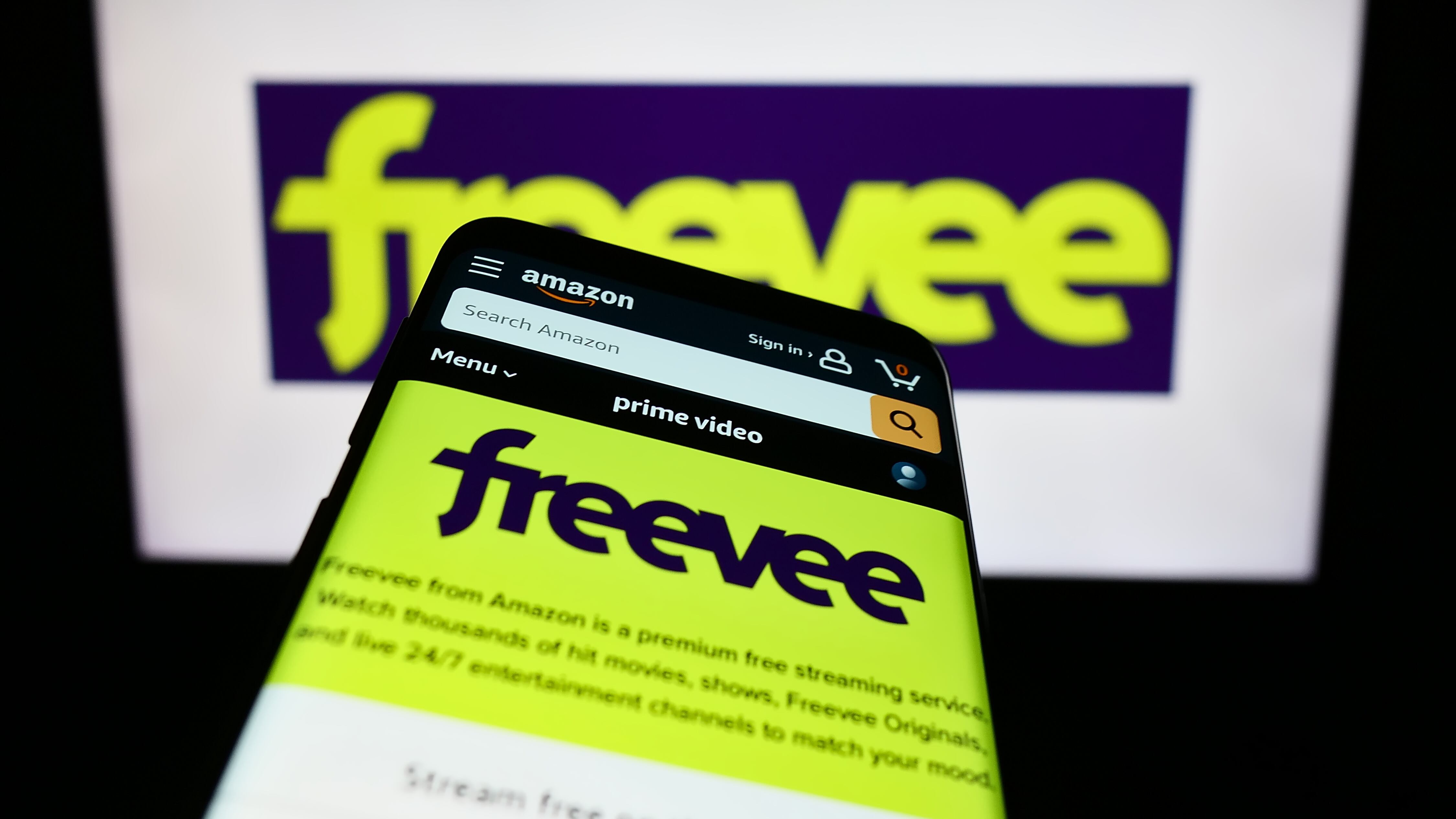 Mobile phone with website of US video-on-demand streaming service Amazon Freevee in front of business logo. Focus on top-left of phone display.